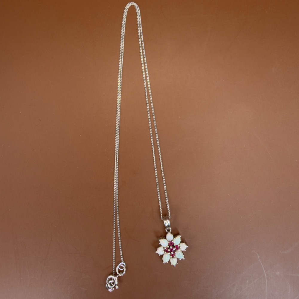 A 9ct white gold chain and cluster pendant featuring central red rubies surrounded by pear-shaped opals in a floral design. View IX