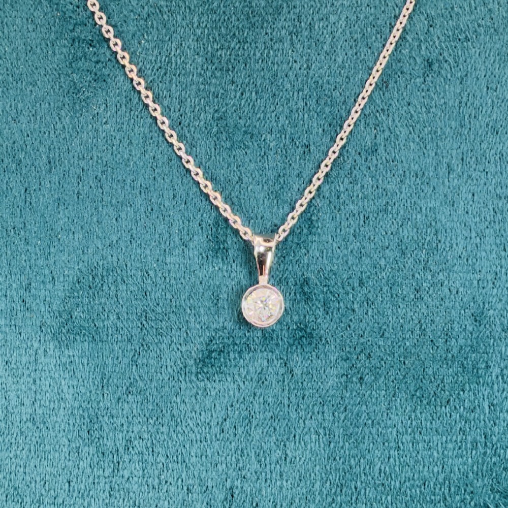 A single round brilliant-cut diamond set in a white gold bezel pendant suspended from a fine white gold chain. View II