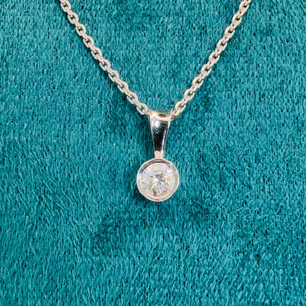 A single round brilliant-cut diamond set in a white gold bezel pendant suspended from a fine white gold chain. View III