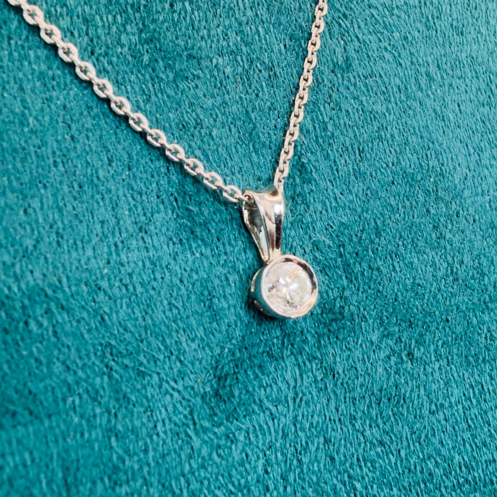 A single round brilliant-cut diamond set in a white gold bezel pendant suspended from a fine white gold chain. View V