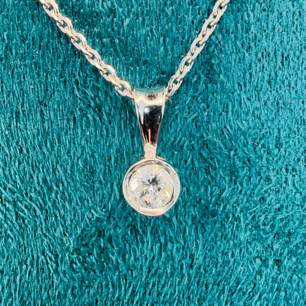 A single round brilliant-cut diamond set in a white gold bezel pendant suspended from a fine white gold chain. View VI