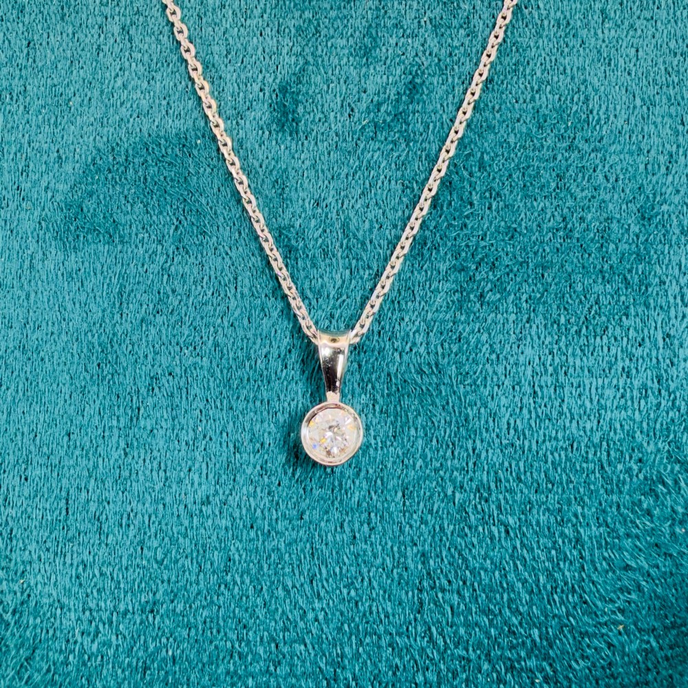 A single round brilliant-cut diamond set in a white gold bezel pendant suspended from a fine white gold chain. View VIII