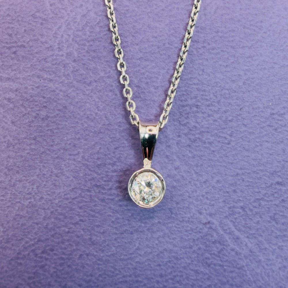 A single round brilliant-cut diamond set in a white gold bezel pendant suspended from a fine white gold chain.