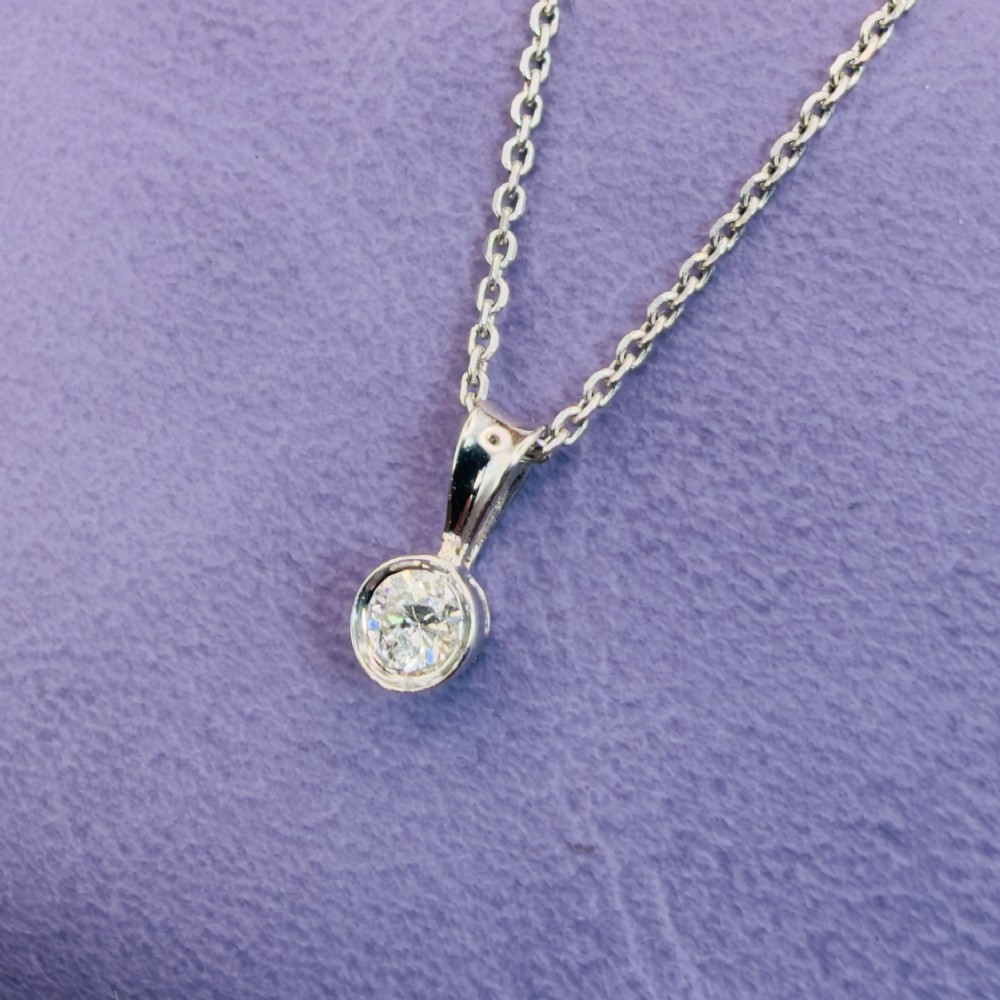 A single round brilliant-cut diamond set in a white gold bezel pendant suspended from a fine white gold chain. View IX