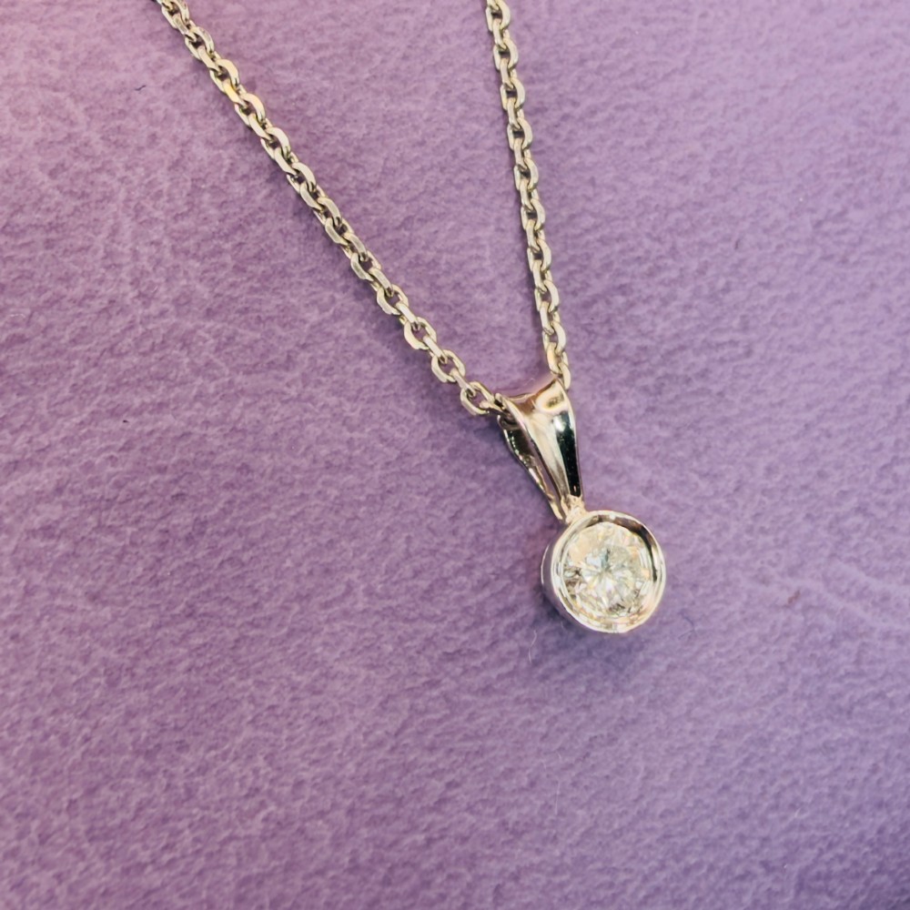 A single round brilliant-cut diamond set in a white gold bezel pendant suspended from a fine white gold chain. View X