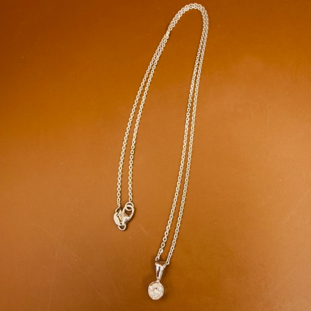 A single round brilliant-cut diamond set in a white gold bezel pendant suspended from a fine white gold chain. View XI