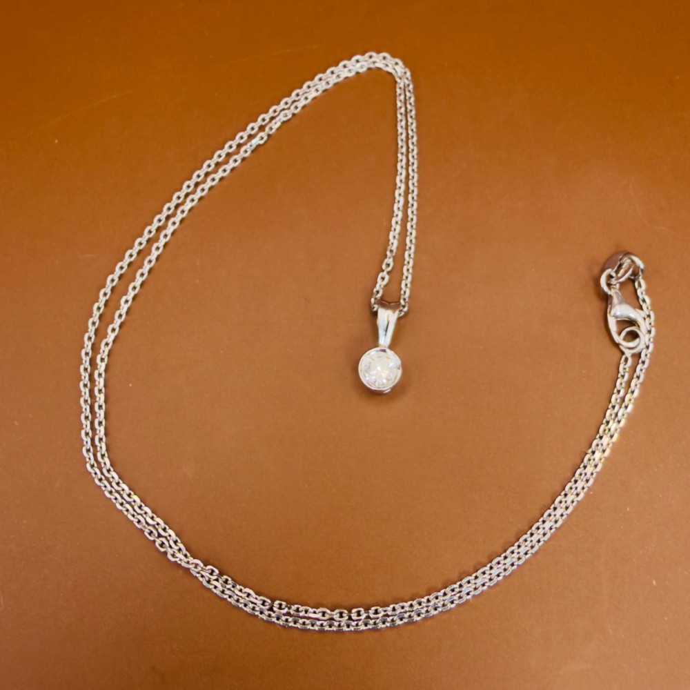 A single round brilliant-cut diamond set in a white gold bezel pendant suspended from a fine white gold chain. View XII