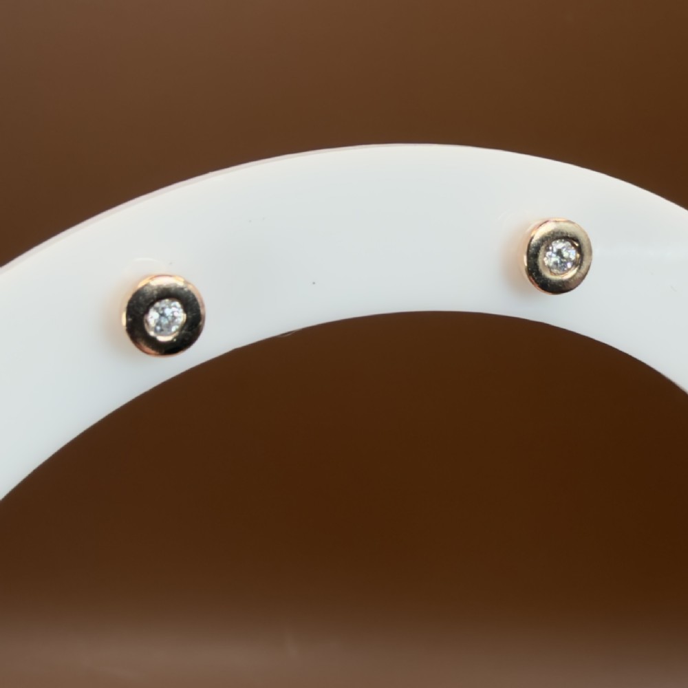 A pair of circular 9ct rose gold stud earrings featuring round bezel-set natural diamonds. View IV