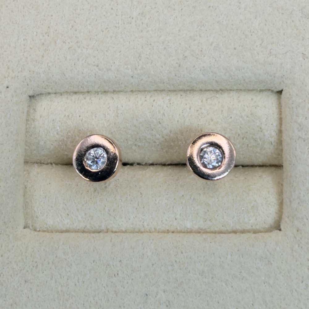 A pair of circular 9ct rose gold stud earrings featuring round bezel-set natural diamonds. View VI