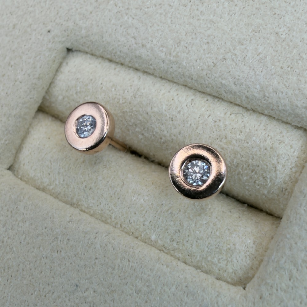 A pair of circular 9ct rose gold stud earrings featuring round bezel-set natural diamonds. View VII