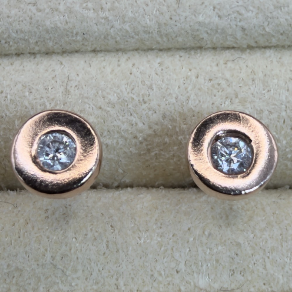 A pair of circular 9ct rose gold stud earrings featuring round bezel-set natural diamonds.