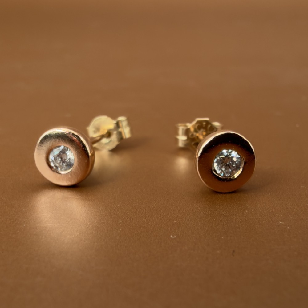 A pair of circular 9ct rose gold stud earrings featuring round bezel-set natural diamonds. View IX