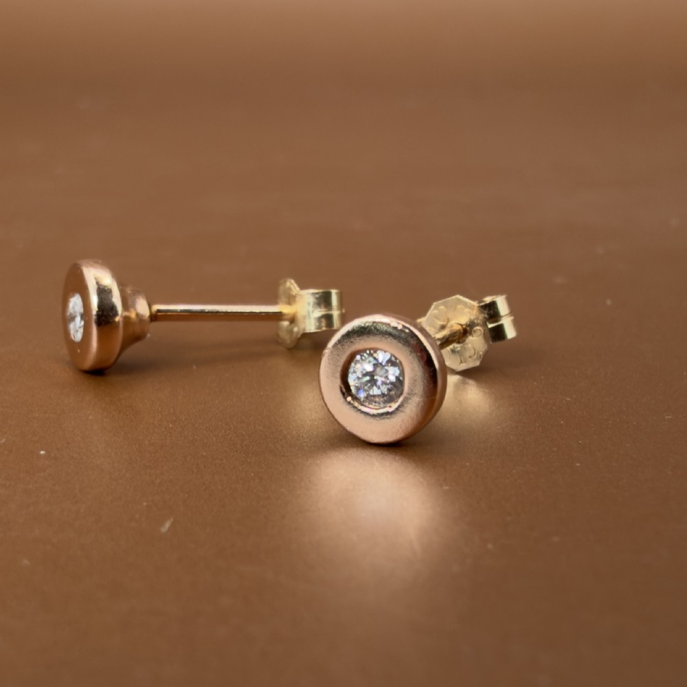 A pair of circular 9ct rose gold stud earrings featuring round bezel-set natural diamonds. View X