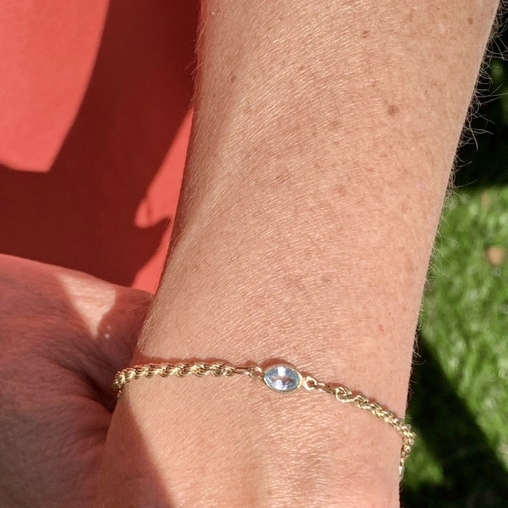 A 9ct yellow gold rope chain bracelet featuring oval bezel-set light blue topaz gemstones at spaced intervals. View II