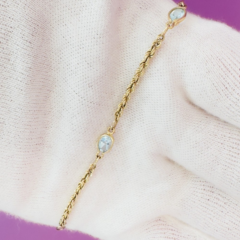 A 9ct yellow gold rope chain bracelet featuring oval bezel-set light blue topaz gemstones at spaced intervals. View IV