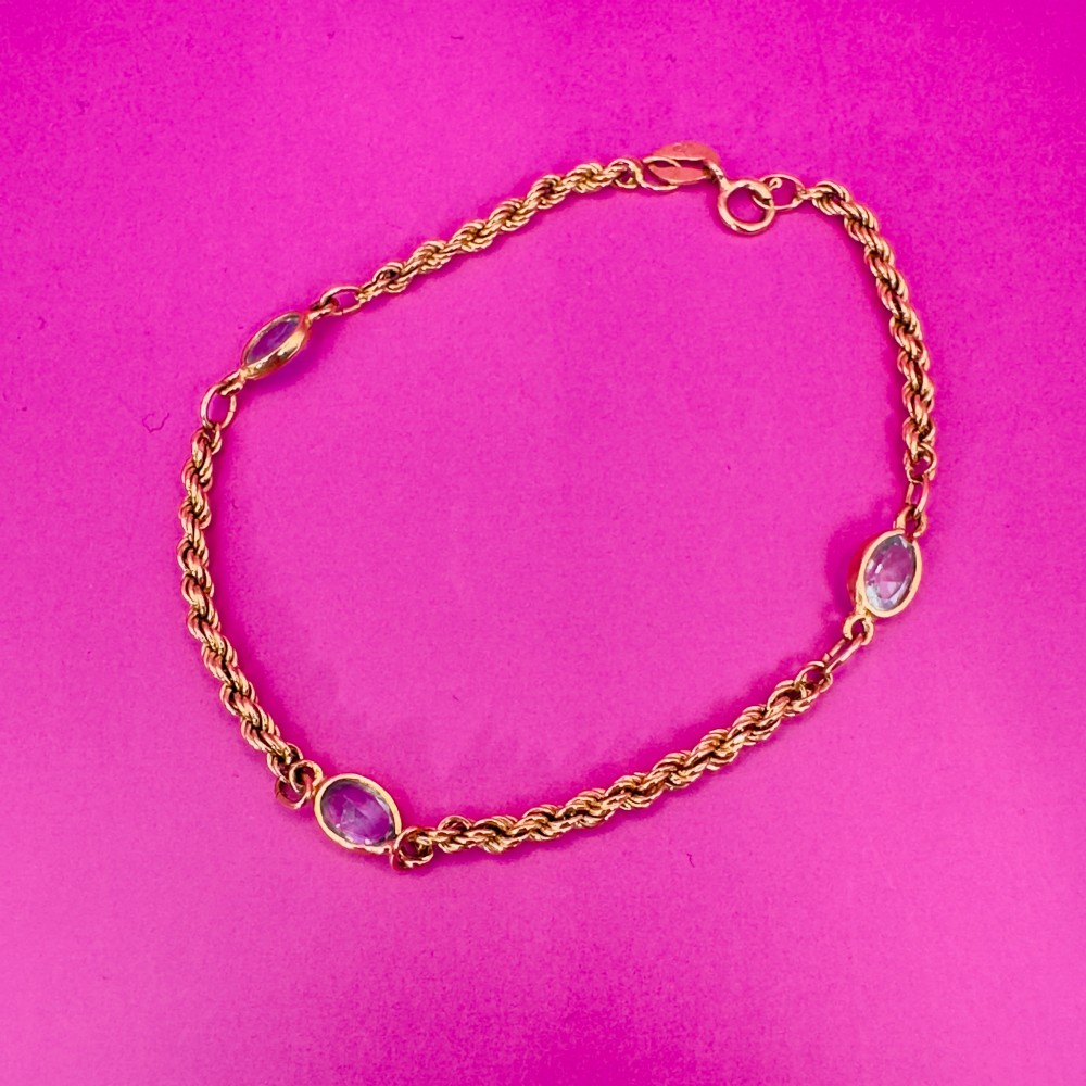A 9ct yellow gold rope chain bracelet featuring oval bezel-set light blue topaz gemstones at spaced intervals. View V