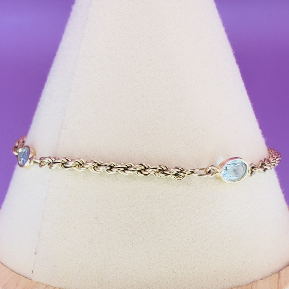 A 9ct yellow gold rope chain bracelet featuring oval bezel-set light blue topaz gemstones at spaced intervals. View IX