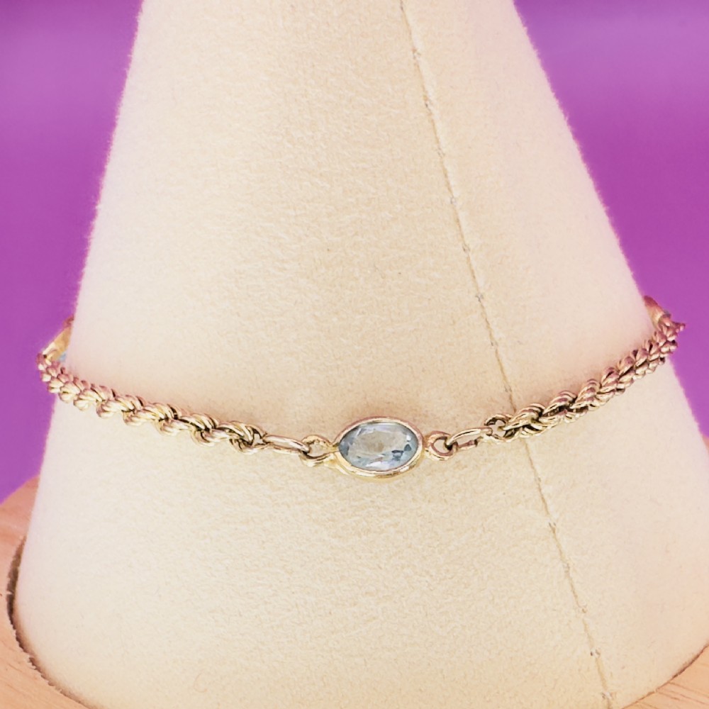 A 9ct yellow gold rope chain bracelet featuring oval bezel-set light blue topaz gemstones at spaced intervals. View X