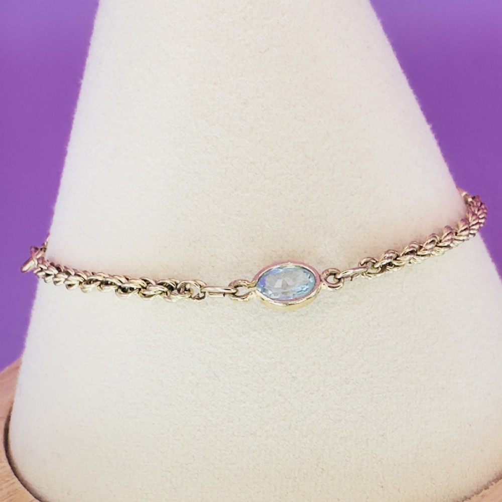 A 9ct yellow gold rope chain bracelet featuring oval bezel-set light blue topaz gemstones at spaced intervals. View XI