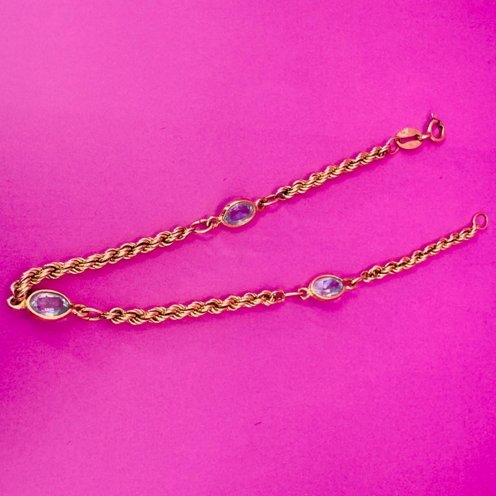 A 9ct yellow gold rope chain bracelet featuring oval bezel-set light blue topaz gemstones at spaced intervals. View VII