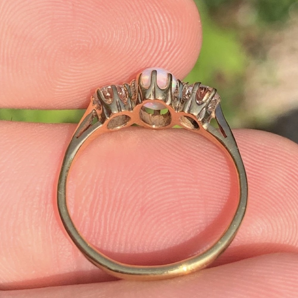 An 18ct yellow gold Art Deco ring featuring an oval cabochon opal flanked by two round diamonds in claw settings. View IV
