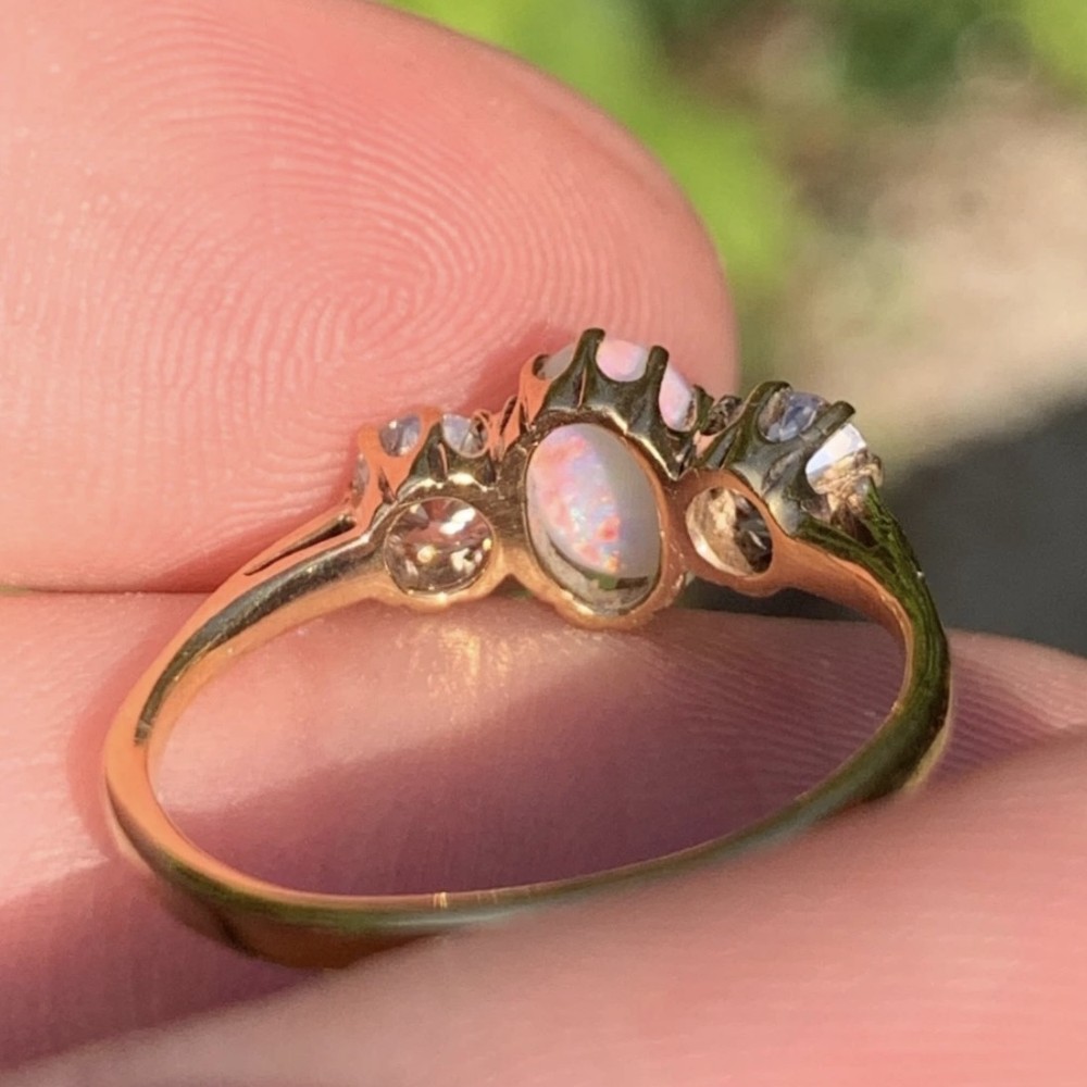 An 18ct yellow gold Art Deco ring featuring an oval cabochon opal flanked by two round diamonds in claw settings. View V