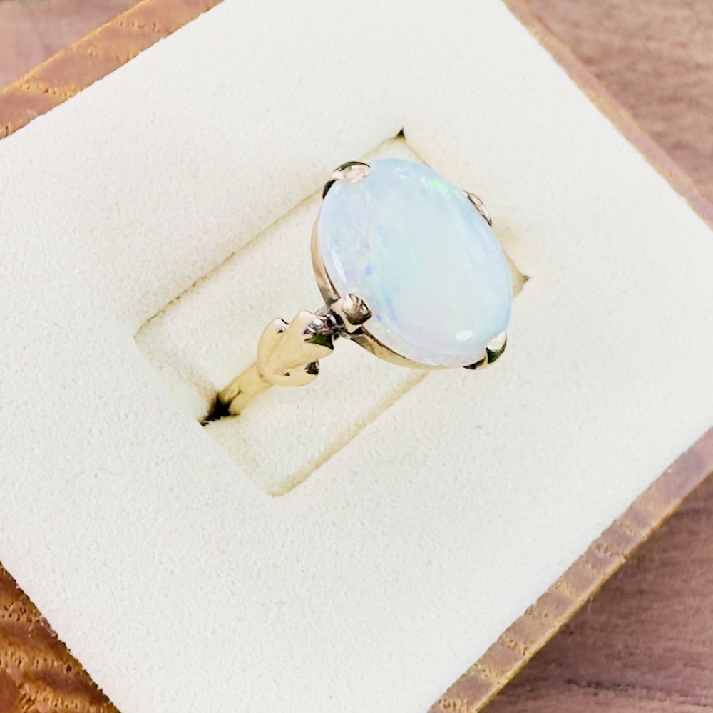 An antique 9ct yellow gold ring featuring a large oval cabochon opal with iridescent flashes held in a claw setting with decorative leaf shoulders.
