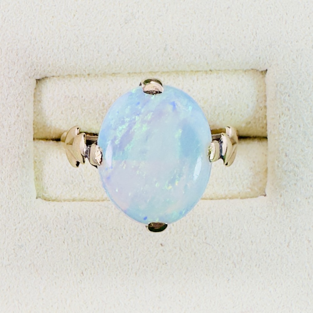 An antique 9ct yellow gold ring featuring a large oval cabochon opal with iridescent flashes held in a claw setting with decorative leaf shoulders. View V