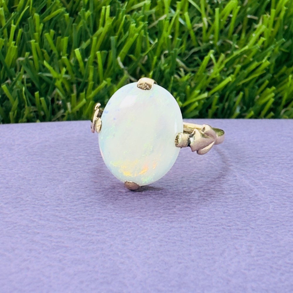 An antique 9ct yellow gold ring featuring a large oval cabochon opal with iridescent flashes held in a claw setting with decorative leaf shoulders. View VI
