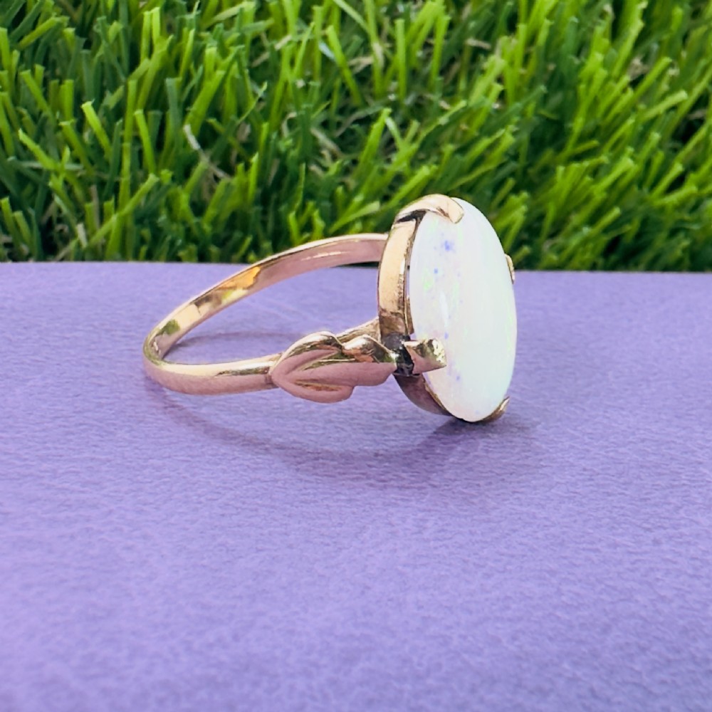An antique 9ct yellow gold ring featuring a large oval cabochon opal with iridescent flashes held in a claw setting with decorative leaf shoulders. View VII