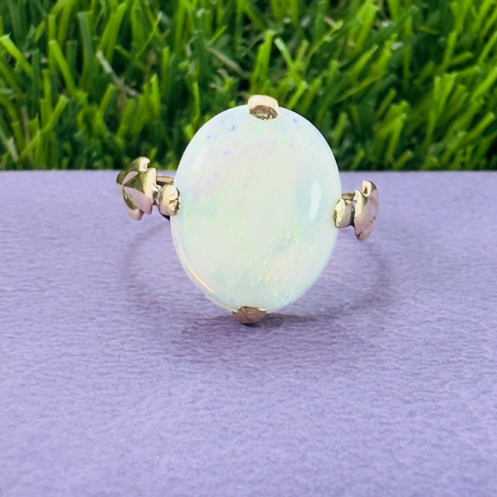 An antique 9ct yellow gold ring featuring a large oval cabochon opal with iridescent flashes held in a claw setting with decorative leaf shoulders. View VIII