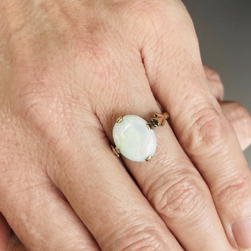 An antique 9ct yellow gold ring featuring a large oval cabochon opal with iridescent flashes held in a claw setting with decorative leaf shoulders. View IX