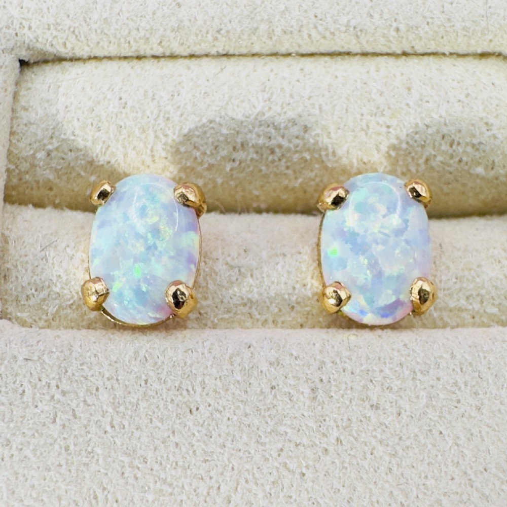 A pair of 14ct yellow gold stud earrings featuring oval-cut white opals held in four-claw settings.