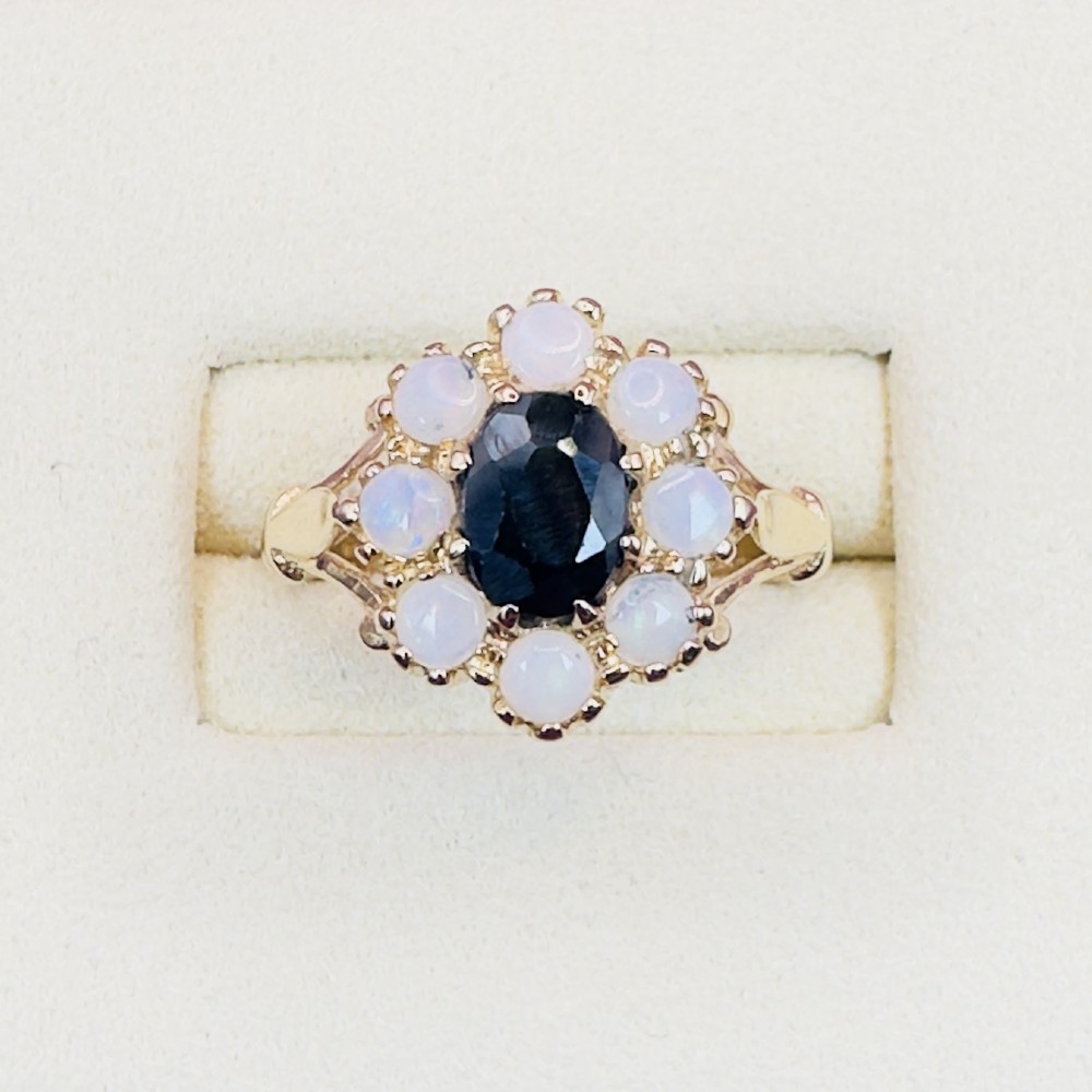 A 14ct yellow gold cluster ring featuring a central oval dark sapphire surrounded by eight white cabochon opals in claw settings. View II