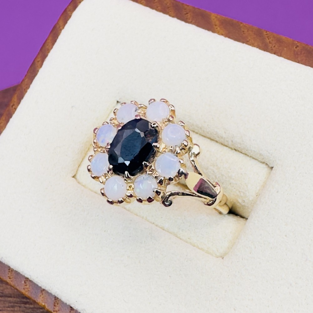 A 14ct yellow gold cluster ring featuring a central oval dark sapphire surrounded by eight white cabochon opals in claw settings. View III
