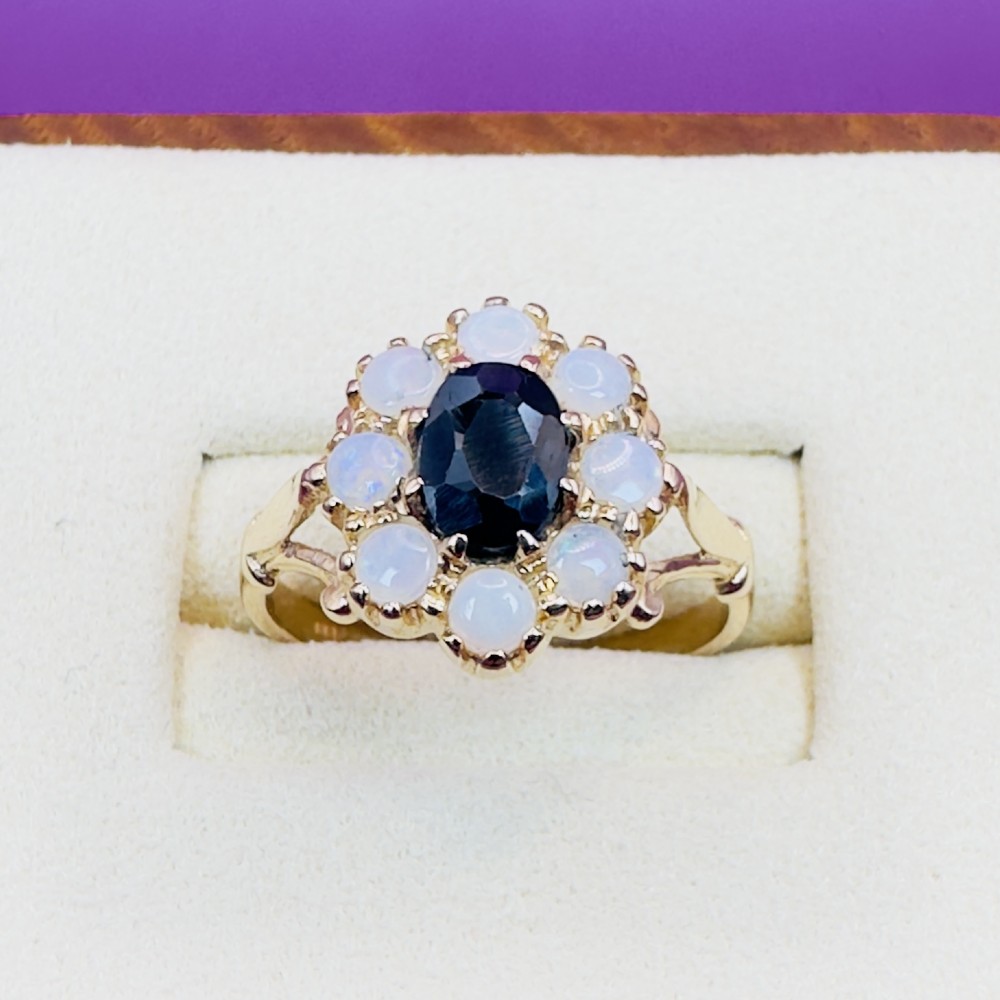 A 14ct yellow gold cluster ring featuring a central oval dark sapphire surrounded by eight white cabochon opals in claw settings. View V