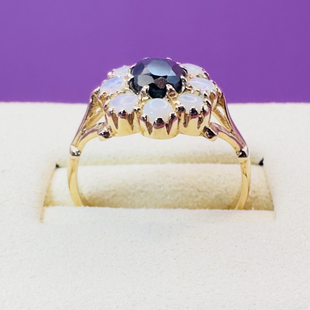 A 14ct yellow gold cluster ring featuring a central oval dark sapphire surrounded by eight white cabochon opals in claw settings. View VI