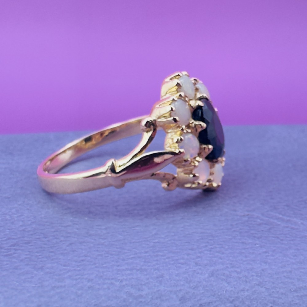 A 14ct yellow gold cluster ring featuring a central oval dark sapphire surrounded by eight white cabochon opals in claw settings. View XI