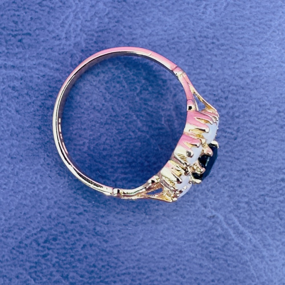 A 14ct yellow gold cluster ring featuring a central oval dark sapphire surrounded by eight white cabochon opals in claw settings. View XII