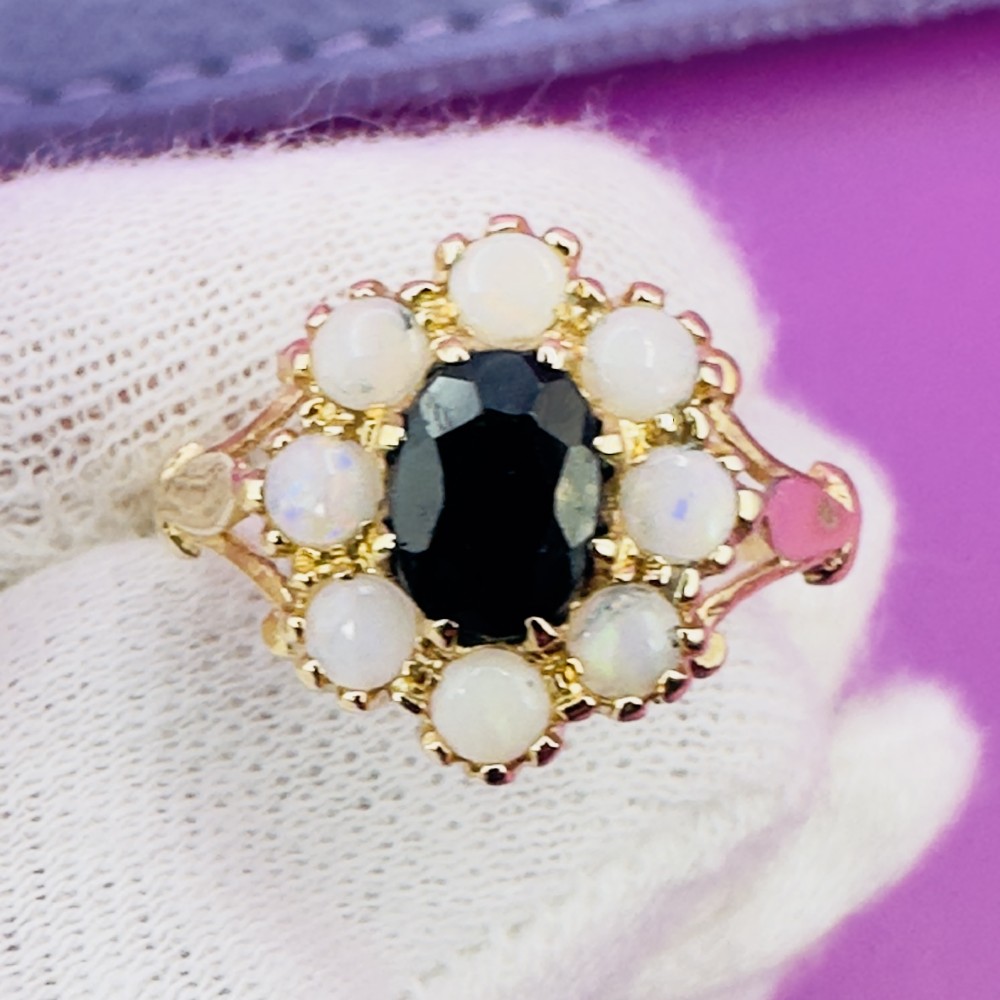 A 14ct yellow gold cluster ring featuring a central oval dark sapphire surrounded by eight white cabochon opals in claw settings. View XIII