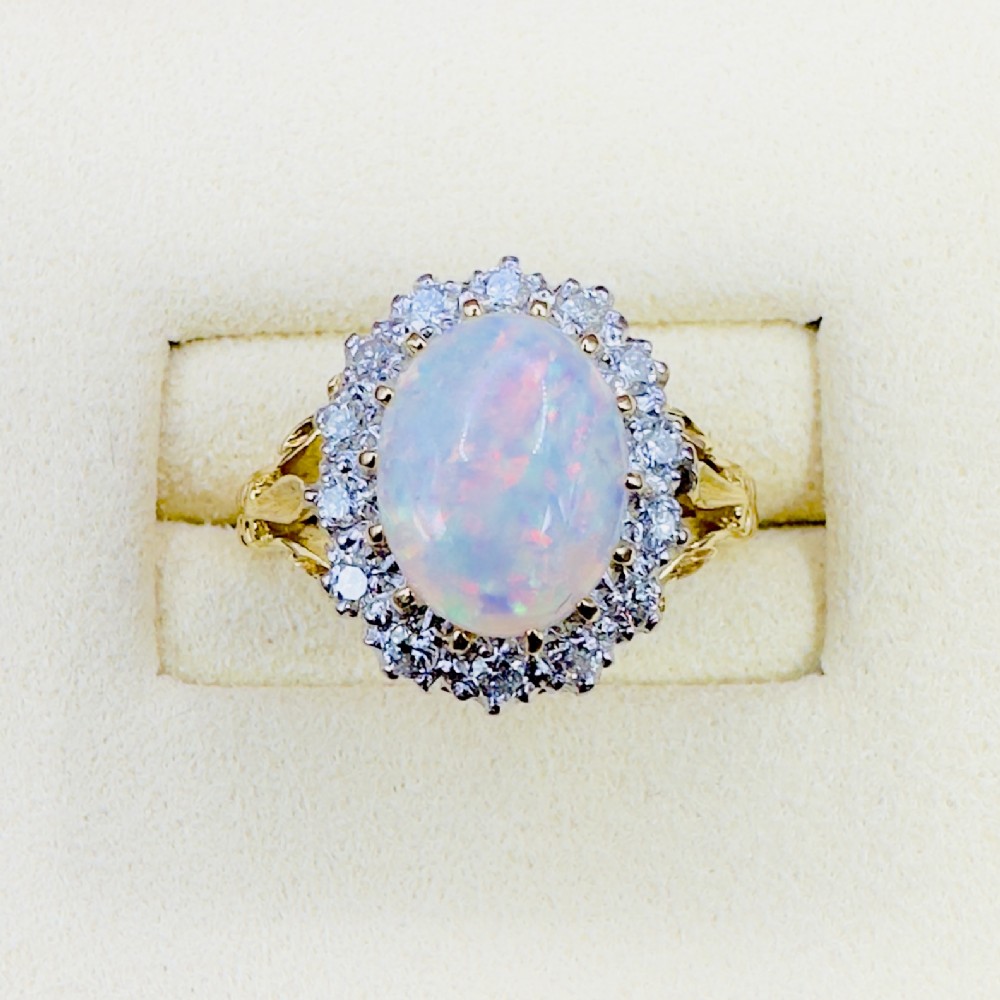 An 18ct yellow gold ring featuring a central oval cabochon opal surrounded by a halo cluster of small round brilliant cut diamonds. View II