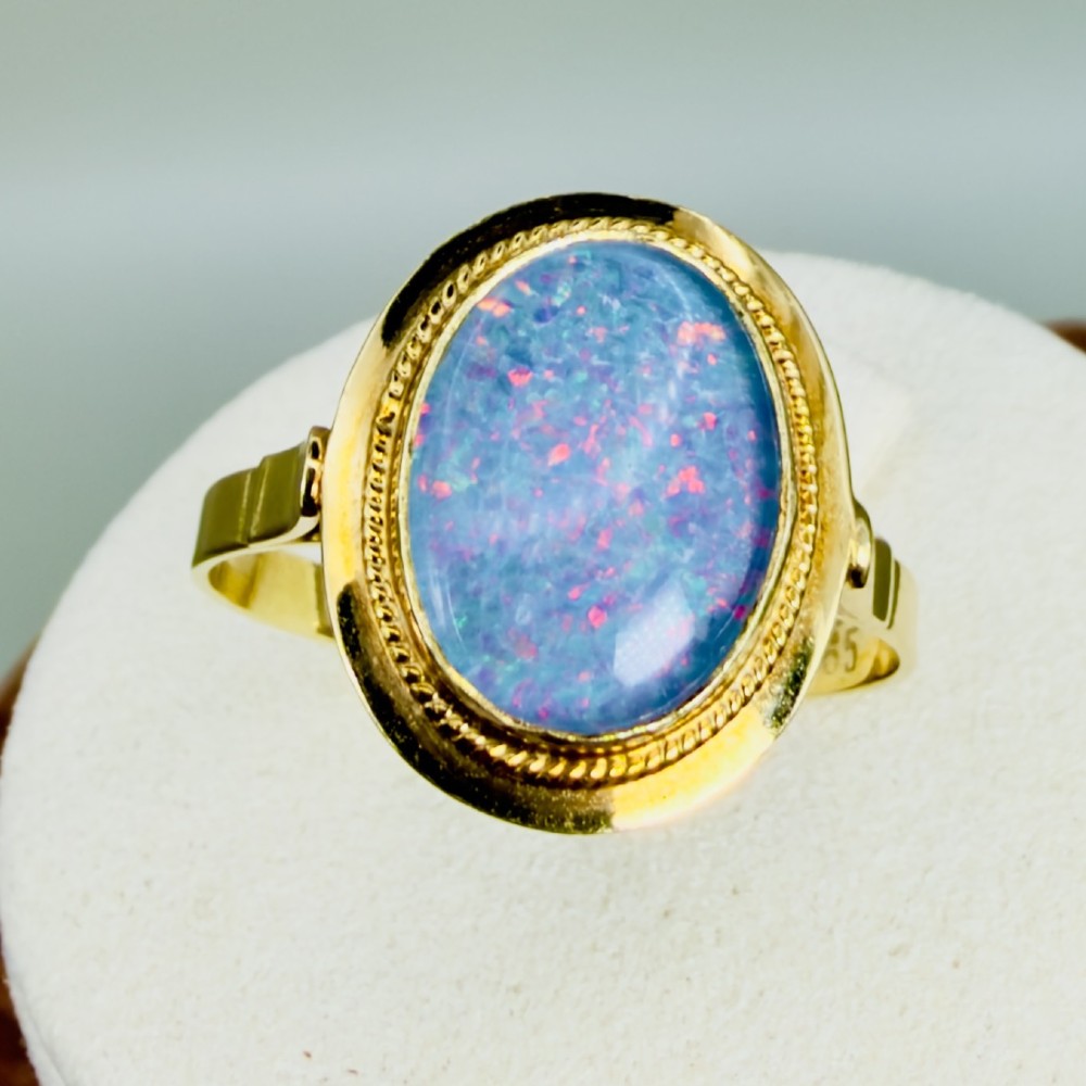 An oval cabochon boulder opal displaying blue and red play of colour set within a 14ct yellow gold ring with a twisted rope border.