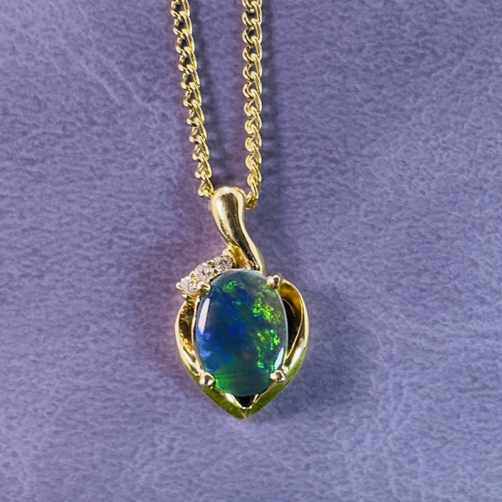 An 18ct yellow gold necklace featuring an oval cabochon black opal displaying green and blue play-of-colour, framed in a contoured gold setting with small diamond accents. View II