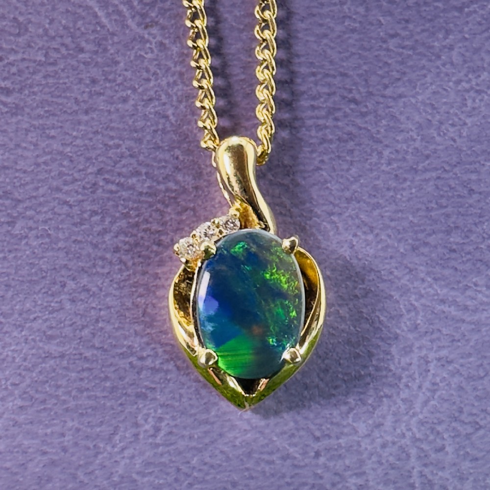 An 18ct yellow gold necklace featuring an oval cabochon black opal displaying green and blue play-of-colour, framed in a contoured gold setting with small diamond accents.