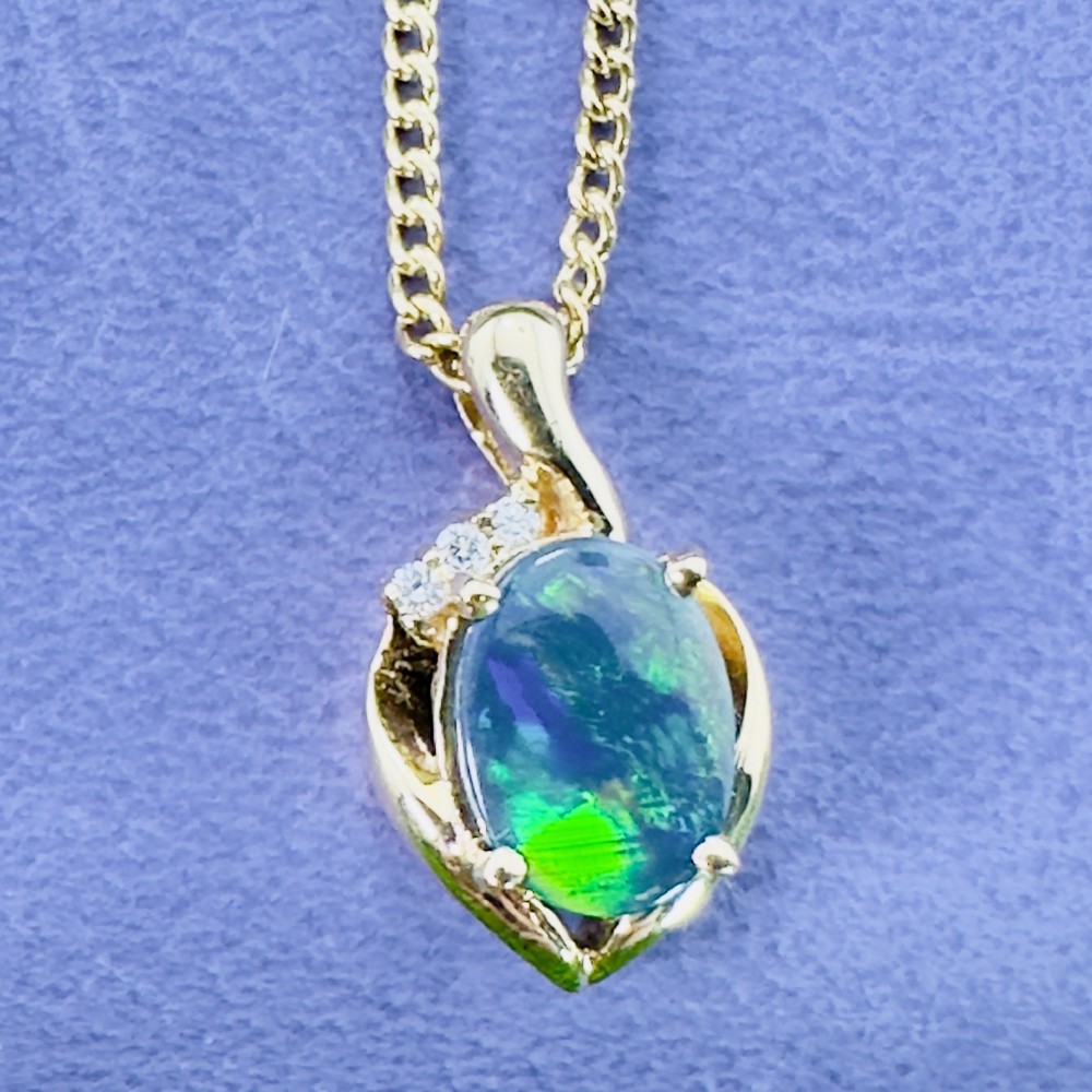 An 18ct yellow gold necklace featuring an oval cabochon black opal displaying green and blue play-of-colour, framed in a contoured gold setting with small diamond accents. View VI