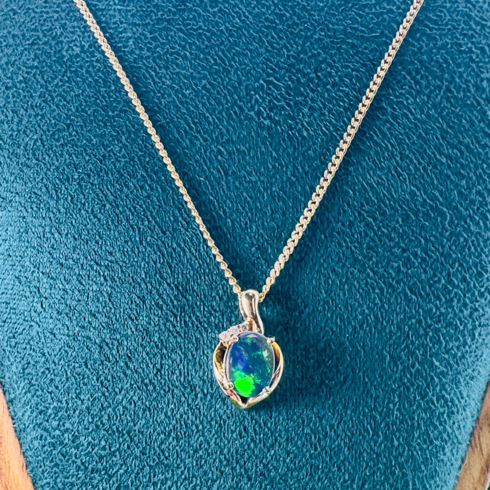 An 18ct yellow gold necklace featuring an oval cabochon black opal displaying green and blue play-of-colour, framed in a contoured gold setting with small diamond accents. View VII
