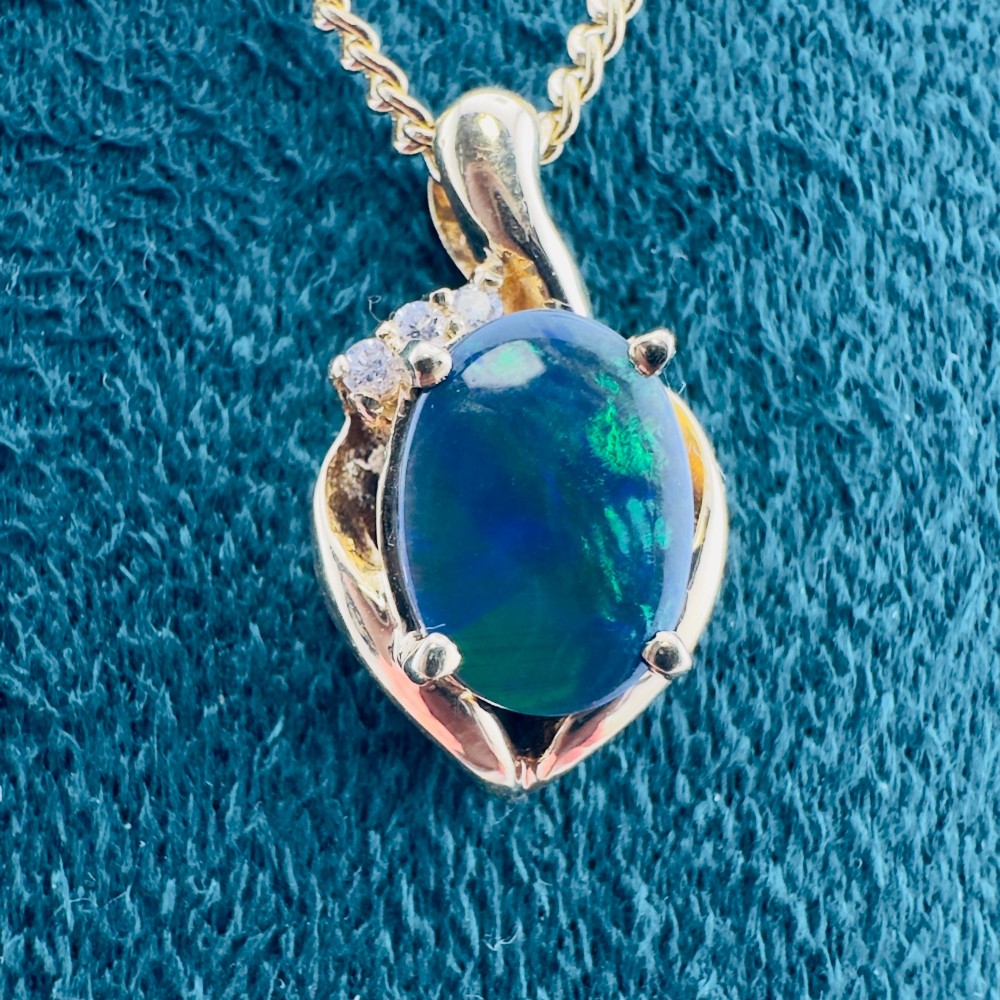 An 18ct yellow gold necklace featuring an oval cabochon black opal displaying green and blue play-of-colour, framed in a contoured gold setting with small diamond accents. View XI
