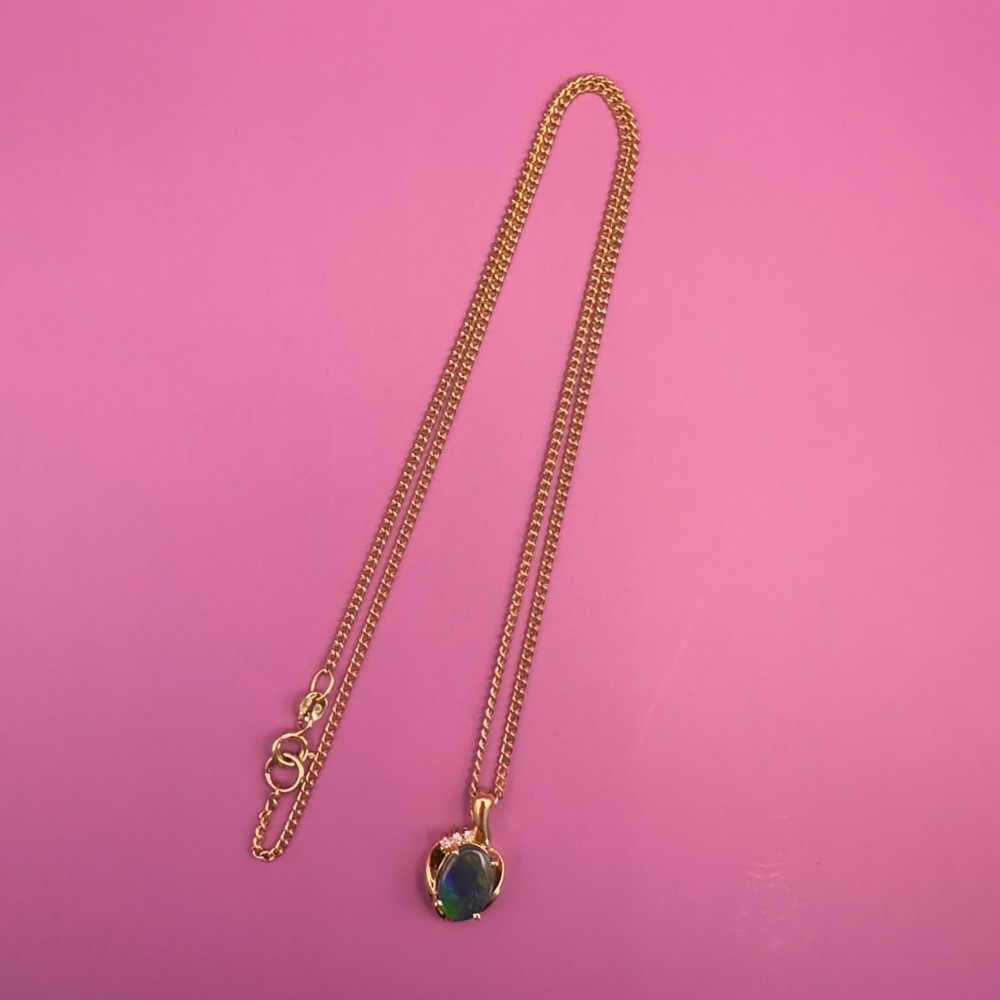 An 18ct yellow gold necklace featuring an oval cabochon black opal displaying green and blue play-of-colour, framed in a contoured gold setting with small diamond accents. View XIV