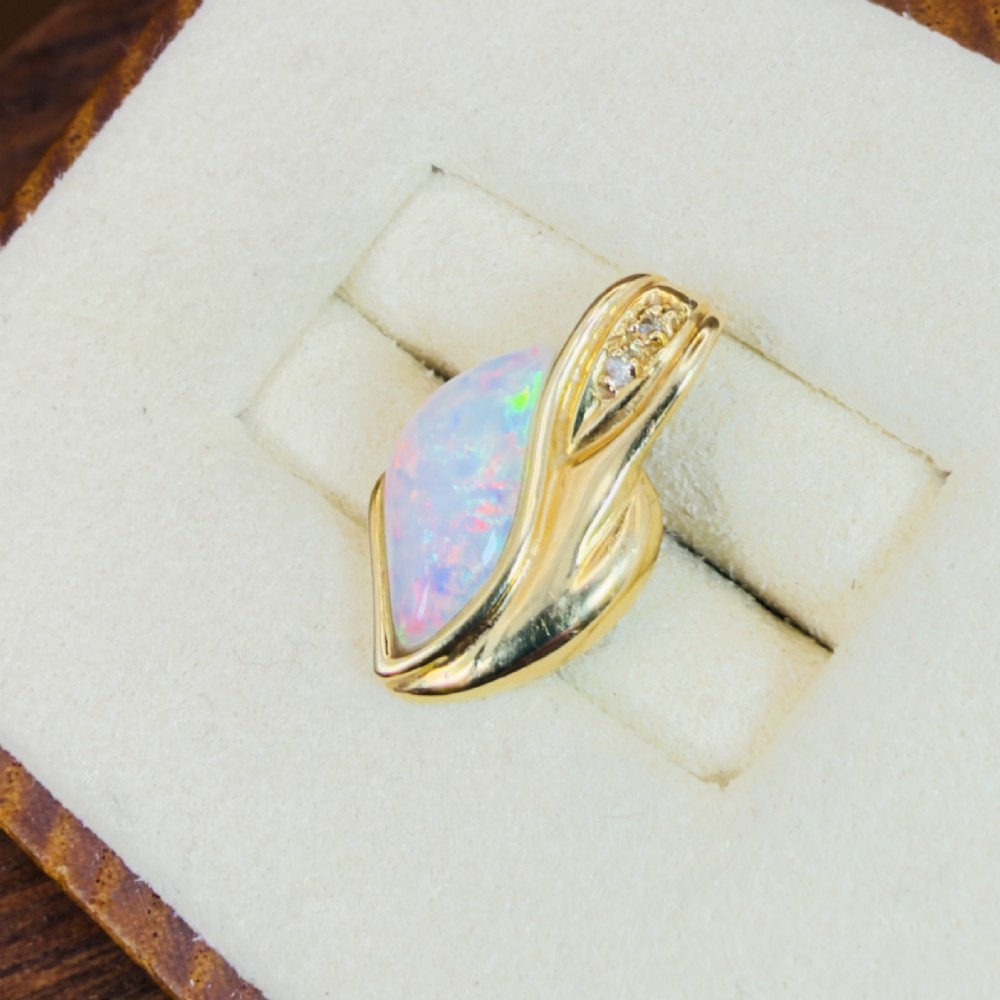 An 18ct yellow gold freeform pendant displaying an iridescent white opal with green and pink flash, set alongside two accent diamonds on the bail. View V