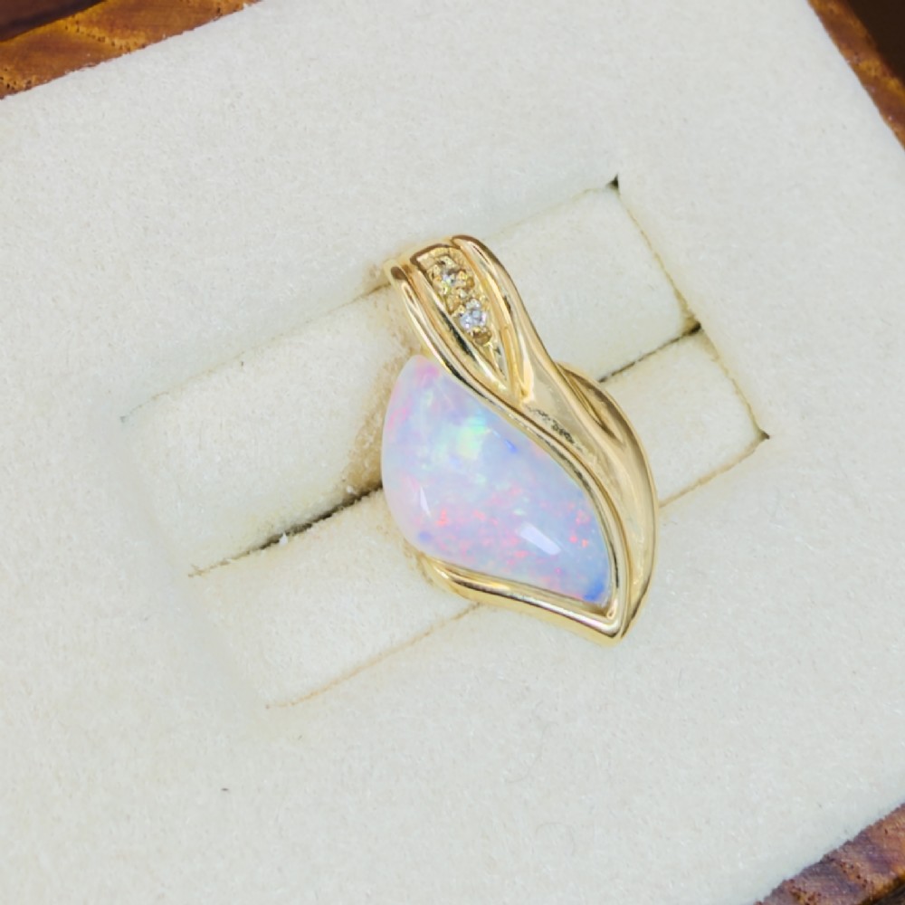 An 18ct yellow gold freeform pendant displaying an iridescent white opal with green and pink flash, set alongside two accent diamonds on the bail. View VI